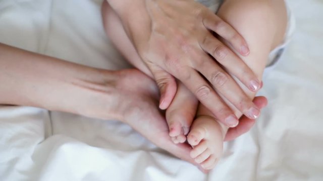 mother touching feet of a newborn baby lying in white bed
