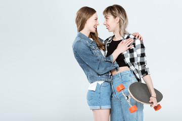 Beautiful young lesbian couple posing together with skateboard isolated on grey