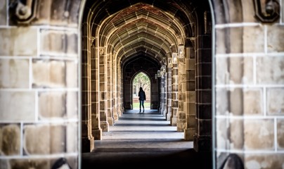 Fototapeta A stone arch hallway at a university with unidentified female in the distance obraz