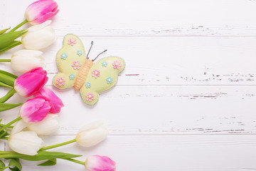 Bright pink and white tulips flowers and decorative butterfly  on  wooden background.