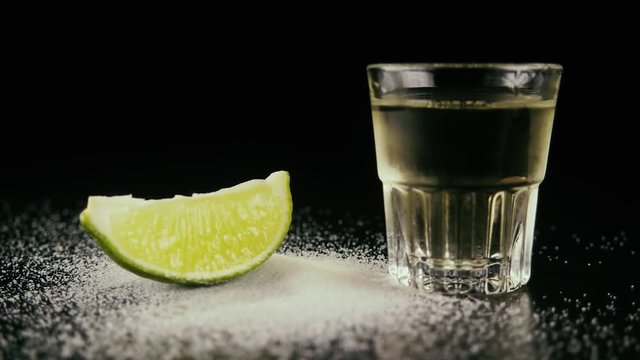 Slow motion. A shot of icy tequila next to the table salt and drops a lime slice