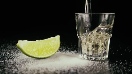 Salt on a table with a lime slice about pour to a shot a tequila. Slow motion