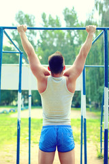 Fototapeta premium Sport, street workout concept - athlete doing pull ups on the horizontal bar outdoors