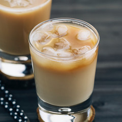 Close-up of a refreshing iced coffee with milk in glasses on a wooden black table.