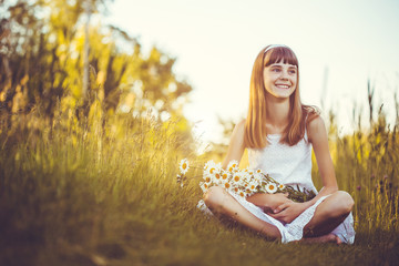 Joyful little girl on a green meadow with a bouquet of chamomiles