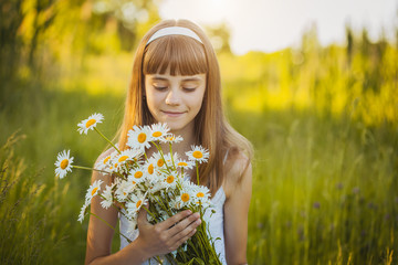 Joyful little girl on a green meadow with a bouquet of chamomiles