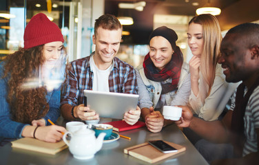 Hard-working managers gathered together in cozy coffeehouse and analyzing results of accomplished work with help of digital tablet