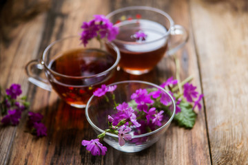 Glass cup of tea on old wooden surface. Small white flowers.