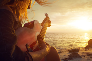 Beautiful young woman playing guitar on sunset beach - obrazy, fototapety, plakaty