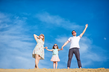 Beautiful happy family walking, running, jumping, having fun along the sand on the beach against the background blue sky in summer vacation