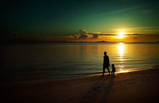 Father and his child walking on sunset beach , silhouette shot and tone image .