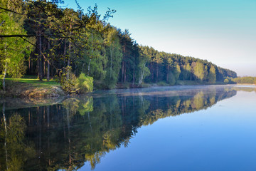 Fototapeta na wymiar Forest and sky reflected in the calm blue water of Lake Forest. Early morning. Relax and silence