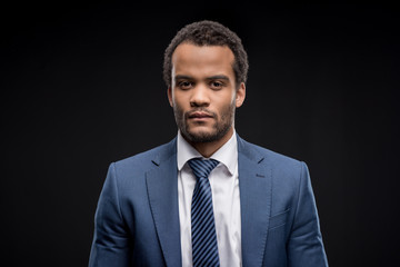 Portrait of confident afro-american businessman in formal wear looking at camera isolated on black