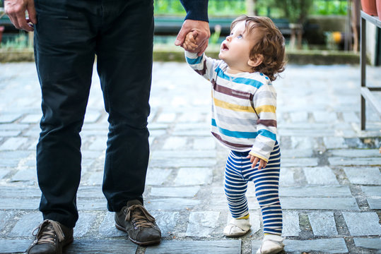 Father and young son, holding hands, low section