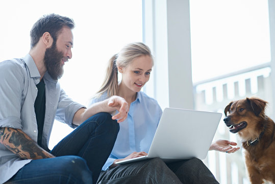 Male and female designers looking at laptop on design studio window seat