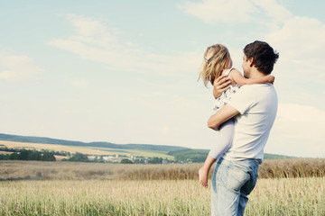 Mature man carrying toddler daughter looking out from wheat field