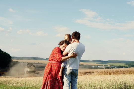 Pregnant couple in wheat field with toddler daughter watching combine harvester