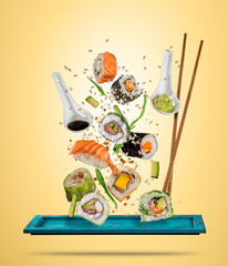 Flying sushi pieces served on plate, separated on colored background