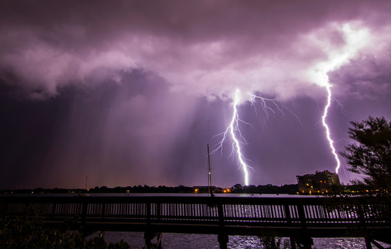 Double bolt of lightning strikes next to a rain shaft over Merritt Island, viewed from the State Road 520 Causeway bridge over Indian River Lagoon, Florida