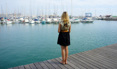 Back view of young woman. She on the pier and looking at yachts and boats