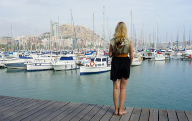 Back view of young woman. She on the pier and looking at yachts and boats