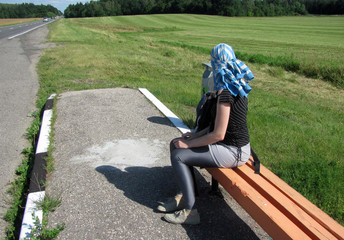 young woman sitting on the bench and waiting for a ride, hitchhiking