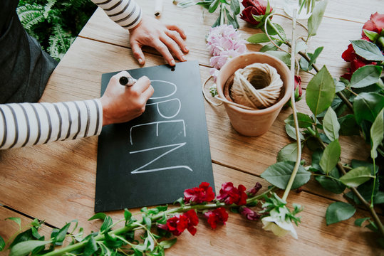 Florist in flower shop, writing 'Open' sign, mid section
