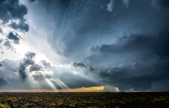 Crepuscular rays through clouds around supercell thunderstorm, as it produces a large tornado just outside of Dodge City, Kansas, on May 24, 2016
