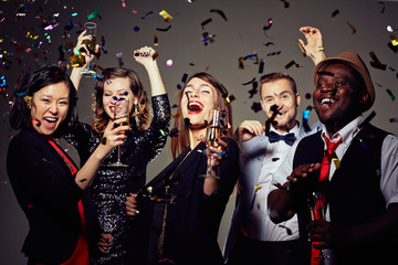 Waist-up portrait of beautiful young woman with champagne flute in hand grinning from ear to ear while celebrating momentous event with best friends © pressmaster