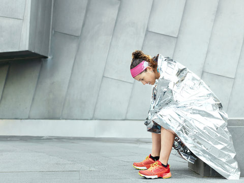 Mature female ultra runner wrapped in foil blanket in city