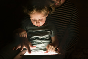 Father with tablet and little daughter at home at night.