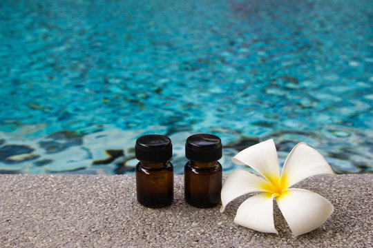 Two bottles of aroma essential oil and flower of frangipani (or plumeria) on the swimming pool background for spa theme.