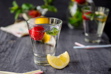 Flavored water with fresh strawberries and mint in glass on a black wooden table with bright details.Selective focus, close up