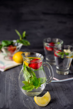 Flavored water with fresh strawberries and mint in glass jars on a black wooden table with bright details.Selective focus, close up. Space for text