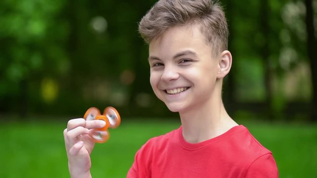 Child having fun outdoors with Spinner. Teen boy showing skills by flicking fidget spinners with finger. Teenager in the summer park.