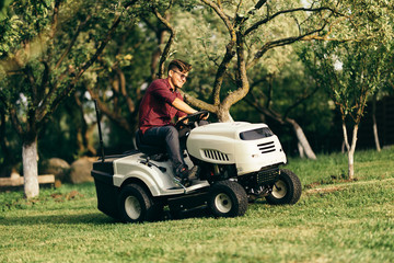 Portrait of handsome man working with lawnmower and driving in garden