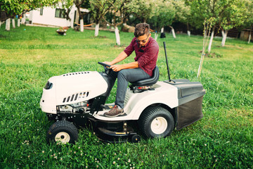 Landscaping details - worker mowing lawn with professional tools in garden