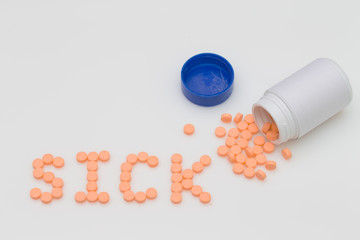 Orange pills spill put of the bottle and arranged in the word Sick.