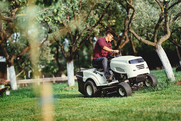 Gardening details with worker using a ride on tractor, mower for cutting grass