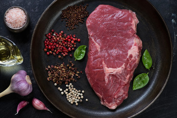Metal plate with raw fresh ribeye beefsteak and seasonings, view from above