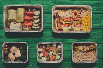 Healthy food take away in boxes, top view at green wood