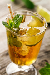 Tasty fresh refreshing summer tea drink with ice, cold tea, lime and mint in glass on wooden background. Closeup.