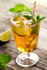Tasty fresh refreshing summer tea drink with ice, cold tea, lime and mint in glass on wooden background. Closeup.