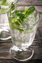 Healthy tasty fresh refreshing detox water in glasses with lime, mint and ice on wooden background. Closeup. Healthy Life Concept.