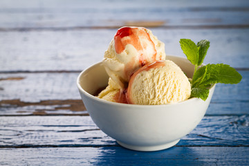 Tasty vanilla ice scoops with strawberry jam and mint in bowl on blue wooden rustic table. Closeup.