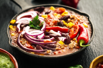 Tasty appetizing mexican food stew in iron pan on dark background closeup.