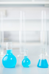 Row of three glass flasks with colored reactant liquid ready for test research on table in modern laboratory
