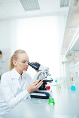 Naklejka na ściany i meble Portrait of beautiful female scientist using microscope working on medical research in modern laboratory