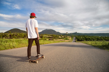 A young guy - a skater in a cap is waiting for a race on a country road
