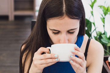 A very beautiful business woman sits in a cafe and holds a cup of coffee in her hands